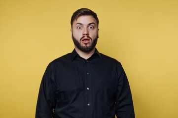 Obraz premium Person shows surprise with wide eyes and mouth open in front of bright yellow background during indoor setting