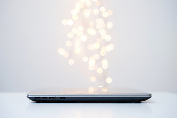 Side view of a dark gray laptop on a white surface with bokeh light effect in the background, for mockup or presentation