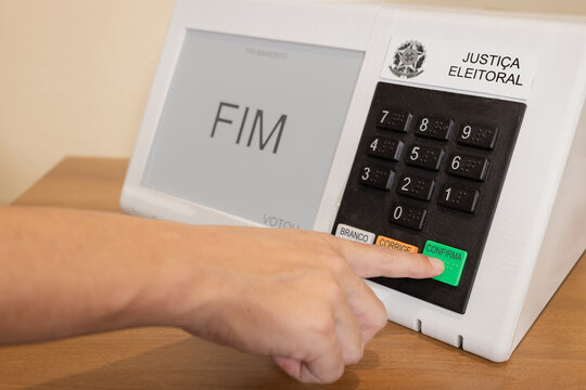 Urna eletr&ocirc;nica brasileira durante elei&ccedil;&otilde;es presidenciais, com eleitor pressionando o bot&atilde;o confirmar. Conceito de democracia, dever c&iacute;vico e processo eleitoral no Brasil.