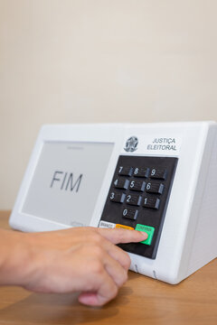 Urna eletr&ocirc;nica brasileira durante elei&ccedil;&otilde;es presidenciais, com eleitor pressionando o bot&atilde;o confirmar. Conceito de democracia, dever c&iacute;vico e processo eleitoral no Brasil.