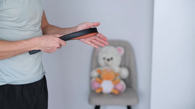 Man holding leather belt for punishment. Hits himself on the hand.
