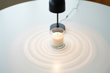 Candle in glass under lamp on white table top