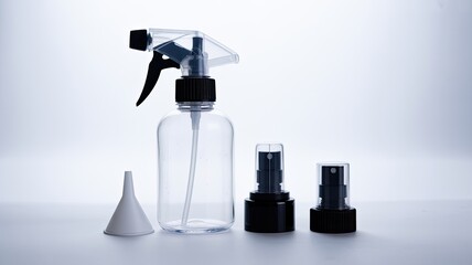 Clear plastic spray bottle with black trigger, two pump tops, and small white funnel for liquids, isolated on white