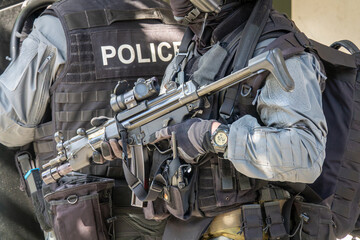 Fototapeta premium Armed SWAT police officer in full tactical gear holding a submachine gun. Special forces soldier on a mission. Law enforcement, counter-terrorism, and security service concept.