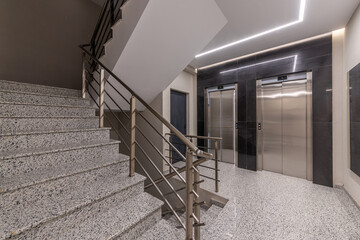 Interior of a modern apartment building hall with staircase and two elevators. Contemporary lobby design in a new residential complex or office. © dechevm