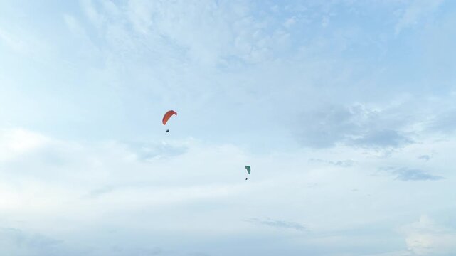 Two paragliders flying together above a green coastline