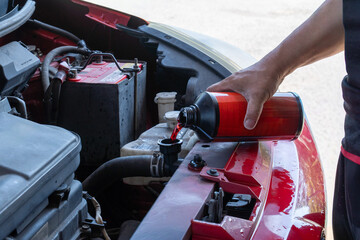 Close up of a hand pouring red coolant into a car's radiator system. Automotive maintenance, DIY vehicle repair, engine cooling, and regular car service concept.