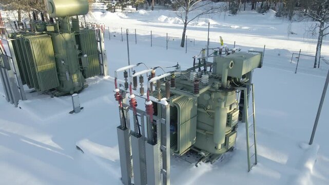 Aerial view of large power transformers at an electrical substation during a freezing winter day, highlighting critical grid infrastructure operating in harsh cold conditions.