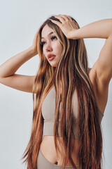 Fototapeta premium Young woman with long hair wearing beige sportswear posing with hands on head, isolated on white background for fitness or beauty concept and lifestyle portrait.