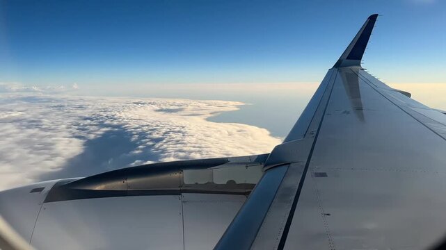 Airplane wing soaring through blue sky and white clouds