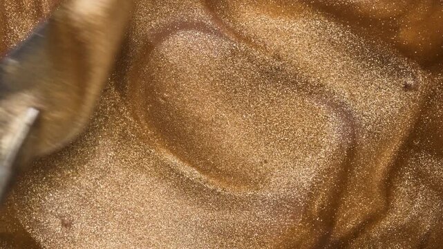 Glowing golden shimmering cosmetic texture of lip gloss mixing with metal spatula. Background for beauty cosmetics