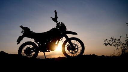 Obraz premium Motorcycle silhouette at sunset, evoking a sense of adventure and freedom against the scenic backdrop. The motorcycle sits silhouetted, with the sun radiating in the background.