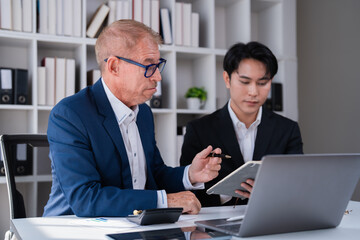 Fototapeta premium Experienced senior businessman providing mentorship and guidance to a young male colleague, discussing business strategy and financial data during a corporate meeting in a modern office environment
