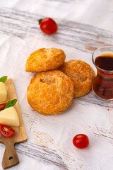 Golden flaky puff pastries served with traditional Turkish tea, fresh cherry tomatoes and sliced cheese on a rustic white wooden table. A cozy homemade bakery and warm light with copy space.