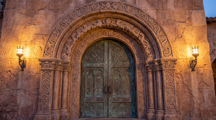 Fototapeta premium Intricate Ancient Stone Archway with Ornate Double Doors, Medieval Architecture Photography, Historic Entrance Facade with Warm Lighting