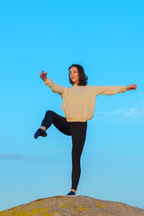 A young woman doing yoga on a rock against a blue sky