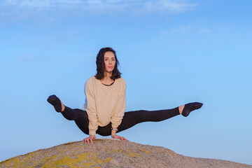 A young woman doing yoga on a rock against a blue sky
