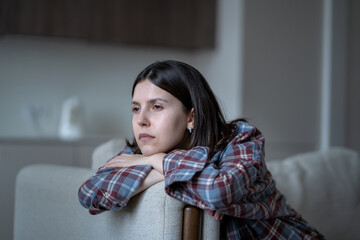 Disinterested bored woman stares blankly out window feeling no motivation, lack of dopamine sits on couch. Lost in thoughts sad girl sits at home alone have low energy. Frustration, apathy, melancholy