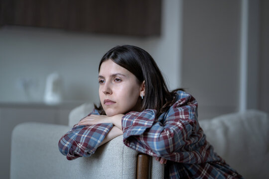 Disinterested bored woman stares blankly out window feeling no motivation, lack of dopamine sits on couch. Lost in thoughts sad girl sits at home alone have low energy. Frustration, apathy, melancholy