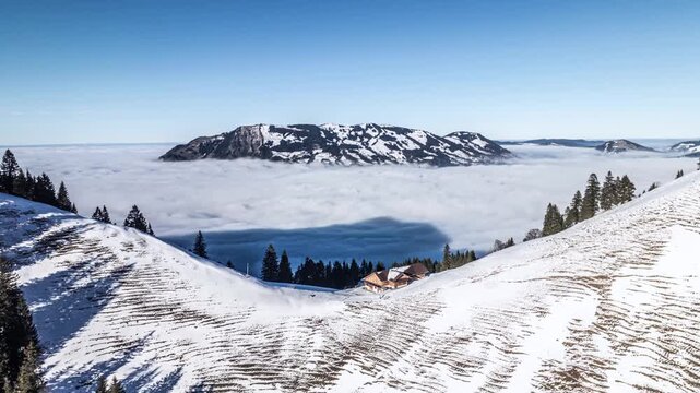 Aerial view of mountain chalet on snowy slope above sa of clouds