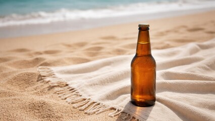 Fototapeta premium A glass bottle of beer rests on a sandy beach, surrounded by a soft blanket, with gentle waves in the background on a sunny day.