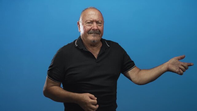 Man pointing finger with right hand and making a strumming fist with left hand in studio against blue wall; playful gesture joy.