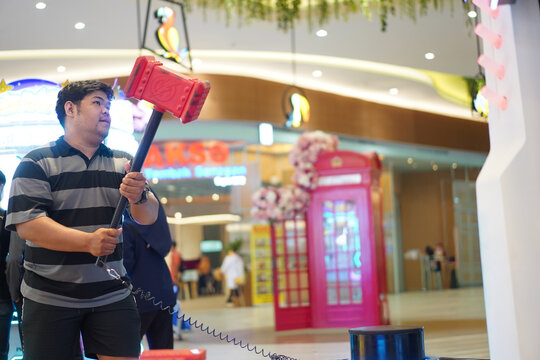Man Lifting Large Red Hammer Toy In Arcade Game Center