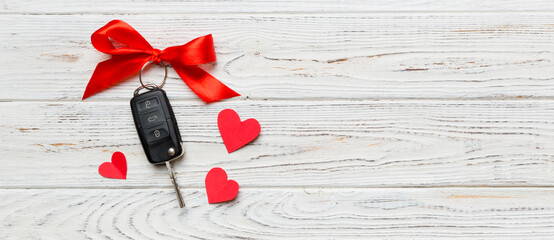 Obraz premium Car key with a red bow and a heart on Colored table. Giving present or gift for valentine day or christmas, Top view with copy space
