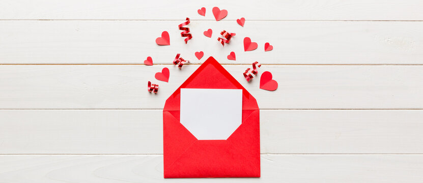 Red paper envelope with empty white card and heart on colored background. top view valentines day concept