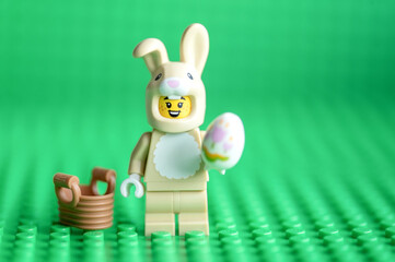 Naklejka premium Lego minifigure Easter bunny with an egg and basket on a green background.