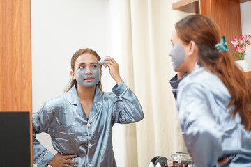 Woman applying detox mud mask to forehead