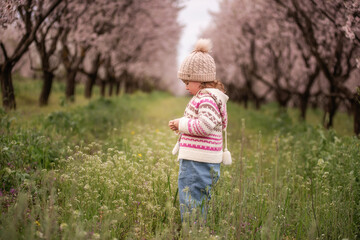 Little girl enjoying spring, playing in a field of wildflowers with thousands of pink cherry blossoms blooming behind, capturing childhood innocence and nature's beauty