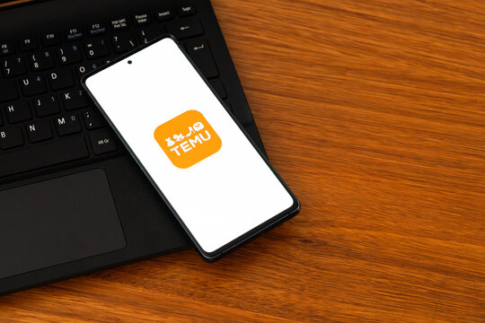 Punta Arenas, Chile &ndash; February 04, 2026: Iconic orange Temu "Shopping Bag" logo on a mobile phone screen resting on a laptop