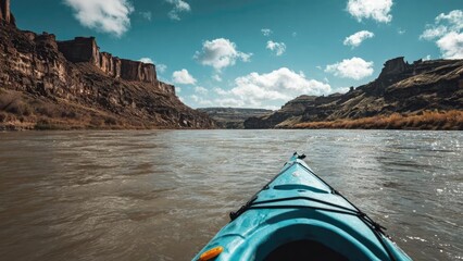 Fototapeta premium From a turquoise kayak, looking down a wide, muddy river flanked by rugged canyon walls under a bright blue sky. Concept Turquoise kayak, muddy river canyon, rugged canyon walls, expansive river