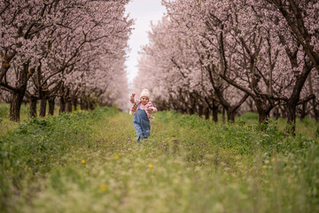 Happy child excitedly running and playing in a vibrant green field between rows of blossoming almond trees, symbolizing childhood joy, freedom, and the beauty of spring nature
