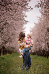 Young mother walking hand in hand with her smiling toddler daughter through a blooming cherry blossom orchard, sharing tender, joyful moments of springtime together