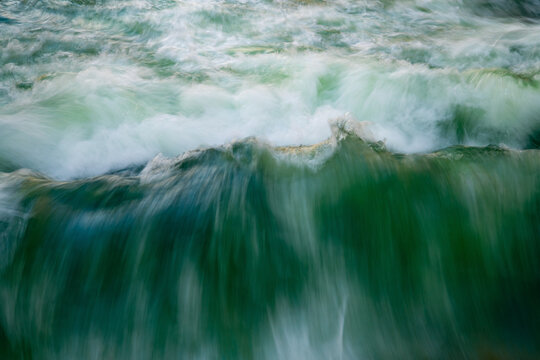 Fast-flowing water captured with long exposure. Colorful greenish, bluish structures, splashes on the famous standing wave of the Eisbach in Munich's English Garden, a popular spot for surfers.