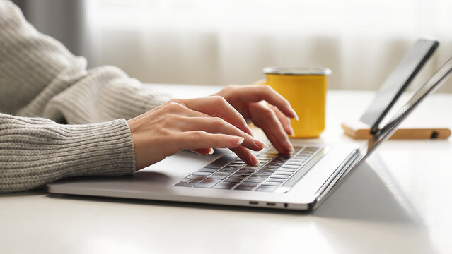 Close-up of woman's hands typing on a laptop at home, working on email, business report, data entry, research, and remote communication for company tasks.