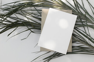 Naklejka premium Blank White Paper Mockup, envelope. Palm Leaves on White Background in Sunlight. Minimal Flat Lay, Natural Shadows. Summer Design for Branding, Wedding, Easter Invitation. Stationery Template.