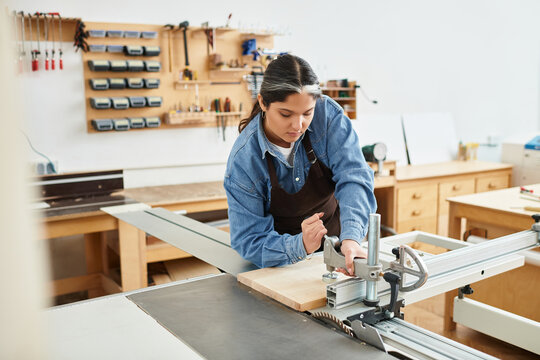 Pretty young woman focuses on her woodworking skills in a bright workshop filled with tools.