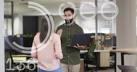 Gesturing man in olive shirt holding laptop, speaking in office, woman in pink top listening, HUD