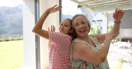 Laughing mom and daughter pressing glass door at home, wearing striped shirt, floral top, watch