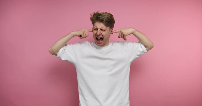 Man shows different facial expressions while holding his ears in front of a pink background