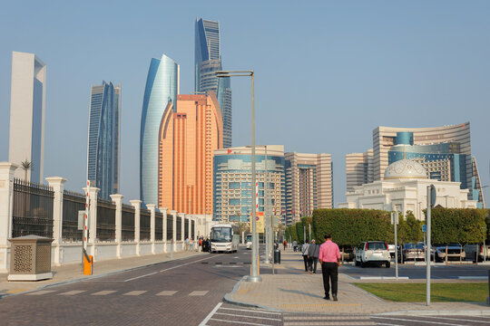 Man walking on a city sidewalk with modern skyscrapers and an arabic building with a dome. Abu dhabi