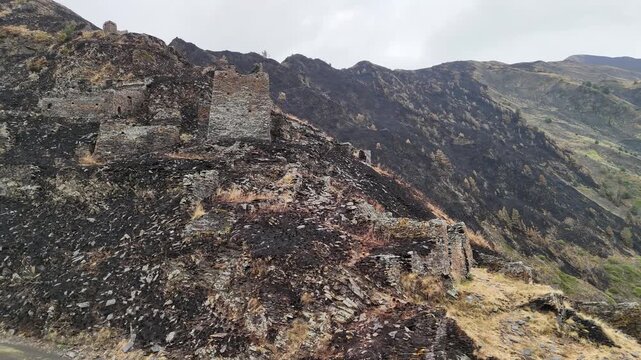Aerial perspective of mutso fortress ruins and towers with a burned hillside landscape, showing the aftermath of a devastating wildfire in the georgian mountains