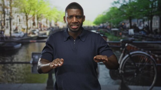 Man hands forward palms down on street by a canal near parked bicycle and bridge, face showing recoil and caution; disgust.