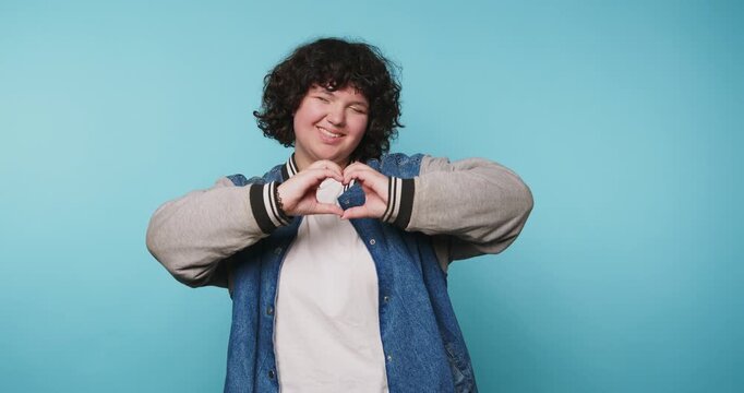 Showing love and joy in front of a blue background with hand gestures at a local studio during an afternoon