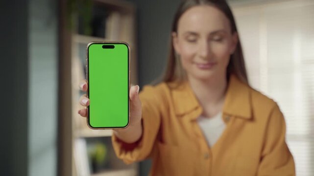 Woman holding a smartphone with a blank green screen display, allowing for the easy insertion of custom content, app interfaces, or promotional material to showcase digital concepts and technology