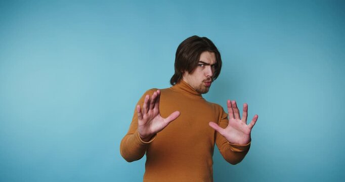 Man makes gestures in front of blue background while wearing a brown sweater and showing different expressions during the interaction