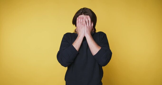 Man covers his face with his hands in a simple yellow background while expressing different emotions in four frames
